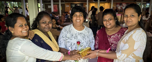 Taru Raj Kumar (center) smiling with four women in India, holding a gift and a red rose together
